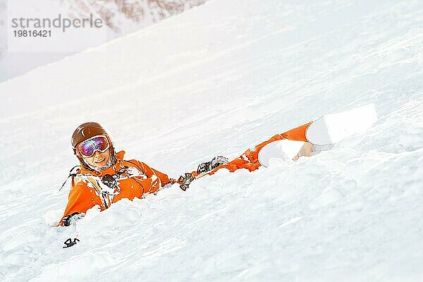 Ein Skifahrer in einem orangefarbenen Overall und mit einem Rucksack liegt nach einem Sturz glücklich im Schnee. Das Konzept der Erholung in den Bergen und des Skifahrens