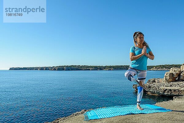 Fitnessfrau mittleren Alters im Freien vor dem Meer macht Yoga Stretching Übungen