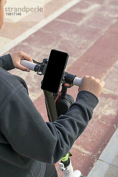 Junger Mann fährt auf einem elektrischen Skateboard im Freien und betrachtet die Route auf einer Smartphone Kartenanwendung  nachhaltiges Verkehrskonzept  grüne Energie ohne CO2emissionen