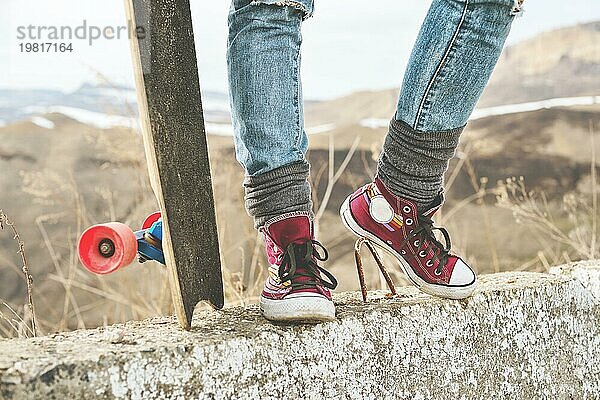 Nahaufnahme von Frauenbeinen in Jeans und Turnschuhen neben einem Longboard oder Skateboard