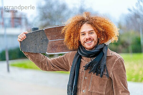 Porträt einer rothaarigen Skaterin  die einen Skateboard trägt und in die Kamera lächelt  in einem Stadtpark