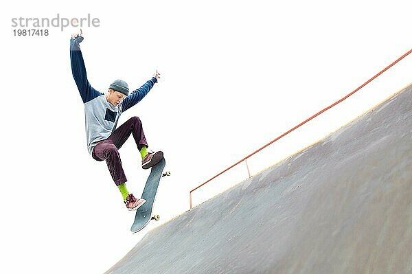 Der Teenager Skateboarder in der Mütze macht einen Trick mit einem Sprung auf der Rampe im Skatepark. Isolierte Skater und Rampe auf weißem Hintergrund