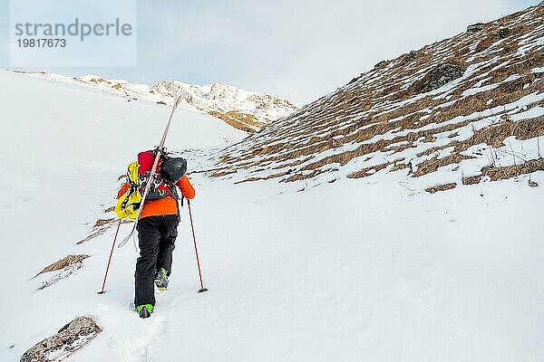 Der Ski Freerider klettert den Hang im Tiefschnee hinauf  wobei die Ausrüstung auf dem Rücken am Rucksack befestigt ist. Das Konzept des Winter Extremsports