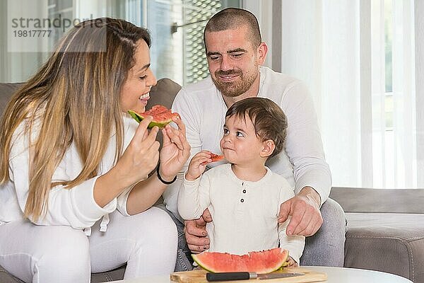 Neue Erfahrungen für einen kleinen Jungen  der mit seinen Eltern im Wohnzimmer eine Wassermelone probiert