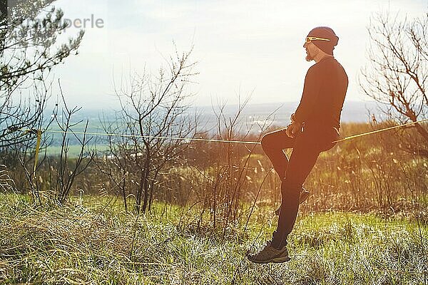 Ein Mann im Alter von auf der Slackline sitzend  das Gleichgewicht haltend und das Leben genießend