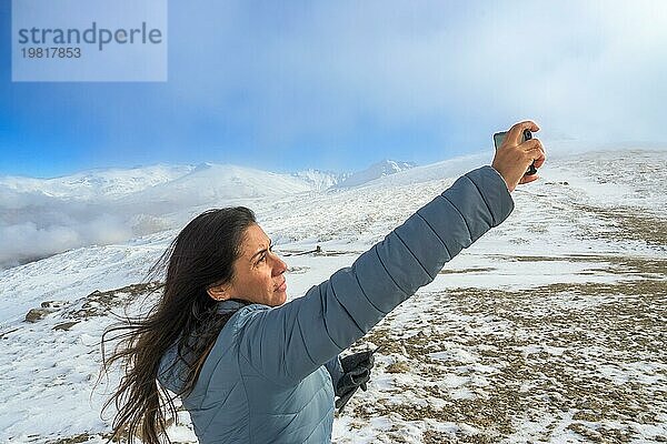 Latina Frau  die ein Selfie mit einem Smartphone macht  während sie einen Wintertag in der Sierra Nevada  Granada  genießt