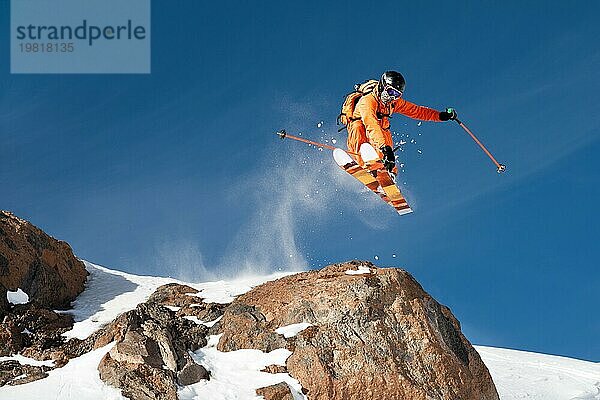 Ein professioneller Skifahrer springt von einer hohen Klippe gegen den blaün Himmel und hinterlässt eine Spur aus Pulverschnee in den Bergen. Foto von den Hängen des Berges Elbrus. Das Konzept des Extremsports und der Erholung in den Bergen im Winter. Kopieren Sie den Raum