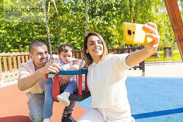 Glückliche Familie nimmt Selfie auf einem Spielplatz mit einem kleinen Jungen in einem sonnigen Tag