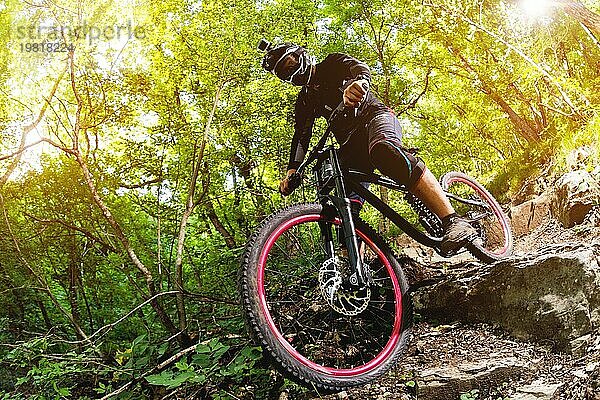 Ein junger Fahrer auf einem Fahrrad für Downhill steigt die Felsen im Wald hinunter