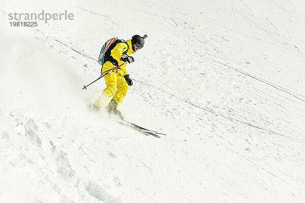 Ein männlicher Freerider mit Bart fährt im Backcountry mit hoher Geschwindigkeit von der Piste ab und hinterlässt eine Spur aus Pulverschnee. Das Konzept der Freeride Kultur und der Backcountry Destinationen im extremen Skisport