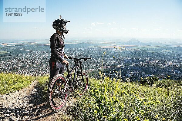 Ein junger Kerl steht auf Ihrem Mountainbike auf einem Berg  wenn unterhalb der Berge niedrige Wolken und Nebel