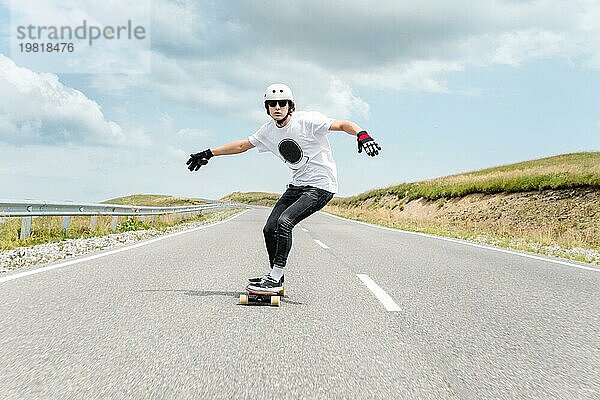 Ein junger Mann mit Helm und Sonnenbrille fährt mit hoher Geschwindigkeit auf einer Landstraße im Regen inmitten von Gewitterwolken