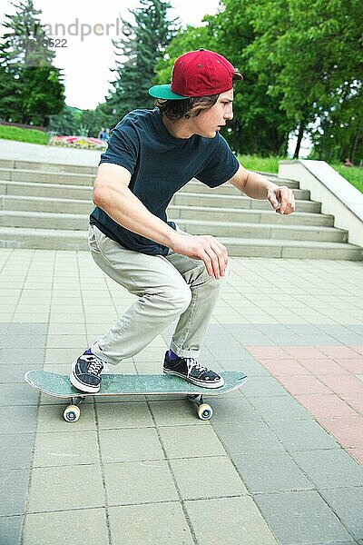 Langhaariger Skater Teenager in TShirt und Turnschuhmütze springt den Ollie vor dem Hintergrund eines stürmischen Himmels über der Stadt