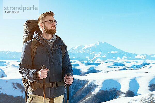 Ein Hipster Reisender mit Bart und Sonnenbrille in der Natur. Ein Mann wandern in den Bergen mit einem Rucksack und skandinavischen Wanderstöcke im Hintergrund eines Berges Elbrus Landschaft und blaün Himmel. Reisen Lifestyle Abenteuer Outdoor Erholung übertreffen