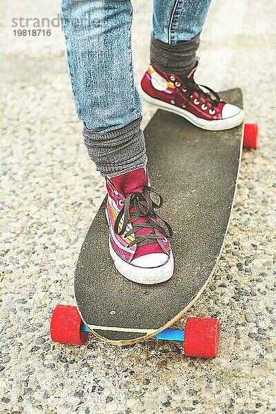 Detail Skateboard teilweise groß mit den Beinen einer Frau in Turnschuhen