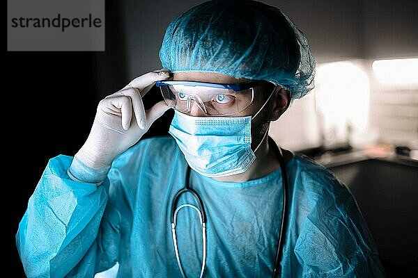 Männlicher Arzt in steriler Uniform und mit Brille  der in einem Labor mit einem Monitor arbeitet