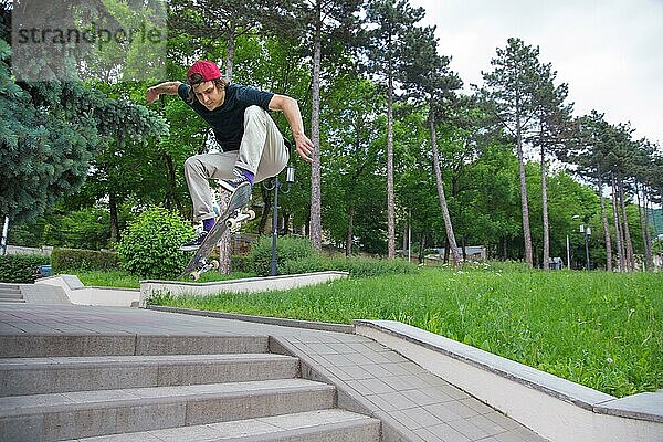 Langhaariger Skater Teenager in TShirt und Turnschuhmütze springt den Ollie vor dem Hintergrund eines stürmischen Himmels über der Stadt