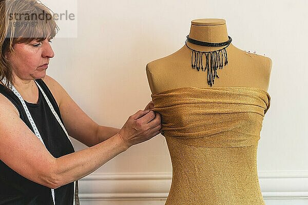Modedesignerin steckt Nadeln in den Stoff einer Schaufensterpuppe