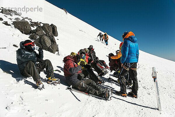 Vollständig ausgerüstete Profi Bergsteiger sitzen bei sonnigem Wetter auf einer verschneiten Piste. Das Konzept der kollektiven Erholung in den Bergen