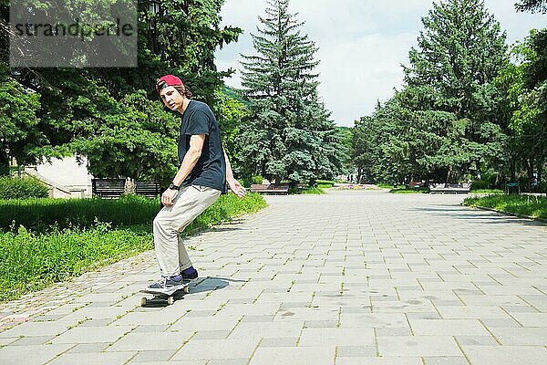 Langhaariger Skater Teenager in TShirt und Turnschuhmütze springt den Ollie vor dem Hintergrund eines stürmischen Himmels über der Stadt