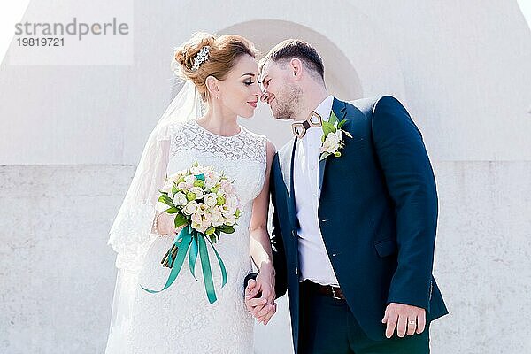 Porträt eines schönen Paares in den Flitterwochen an einem Hochzeitstag mit einem Blumenstrauß in der Hand vor dem Hintergrund eines orthodoxen christlichen Denkmal mit Engeln. Das Konzept der christlichen Hochzeit in der Kirche der Frischvermählten und der spirituelle Glaube der jungen Familie