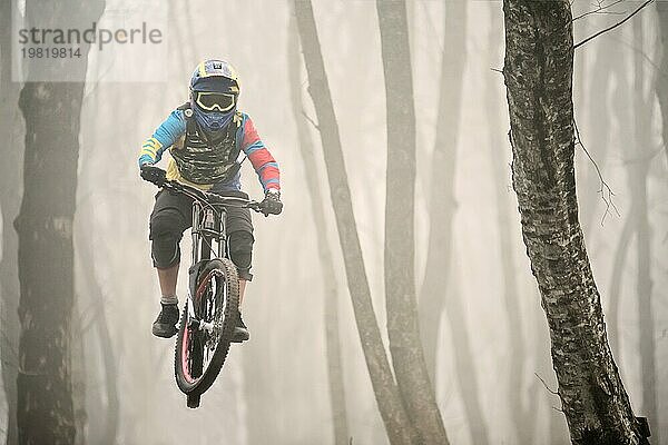 Ein Mountainbikefahrer springt von einem Sprungbrett in einem nebligen Wald  im Kaukasusgebirge  Downhill Fahrer