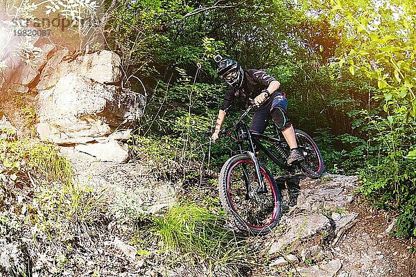 Ein junger Fahrer auf einem Fahrrad für Downhill steigt die Felsen im Wald hinunter