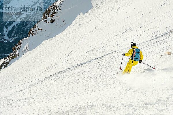 Ein männlicher Freerider mit Bart fährt im Backcountry mit hoher Geschwindigkeit von der Piste ab und hinterlässt eine Spur aus Pulverschnee. Das Konzept der Freeride Kultur und der Backcountry Destinationen im extremen Skisport