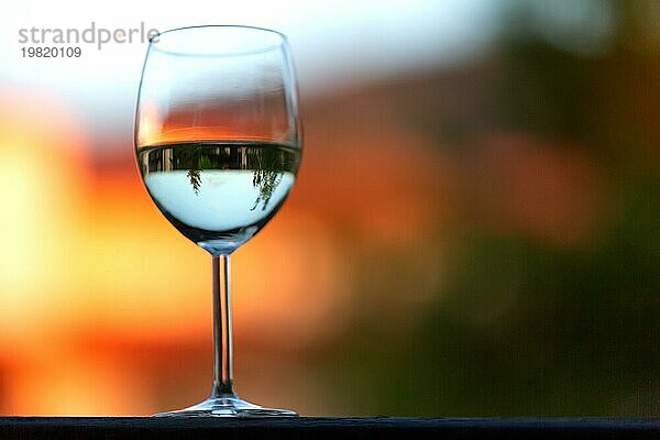 Ein weißes Weinglas auf dem Sonnenuntergang Unschärfe Hintergrund
