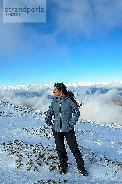 Latina mittleren Alters auf einem schneebedeckten Berg über den Wolken