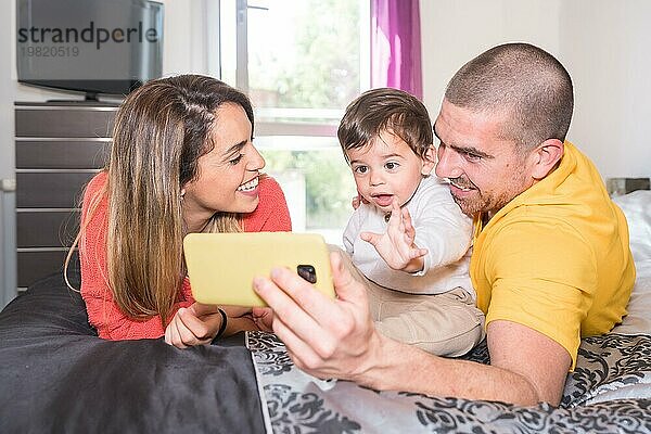 Eltern und kleiner Junge  der ein Mobiltelefon benutzt  liegen zusammen auf dem Bett