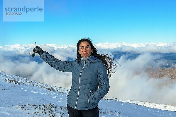 Porträt der lateinischen Frau lächelnd im Schnee  mit warmer Kleidung über den Wolken  auf dem Gipfel des Berges von Sierra Nevada