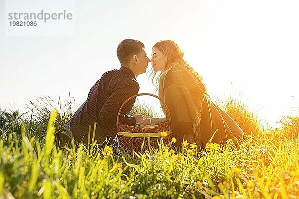 Blick von hinten. Junges Ehepaar küssen auf Picknick in der Natur auf Sonnenuntergang Hintergrund. Das Konzept einer glücklichen jungen Familie und Einheit mit der Natur