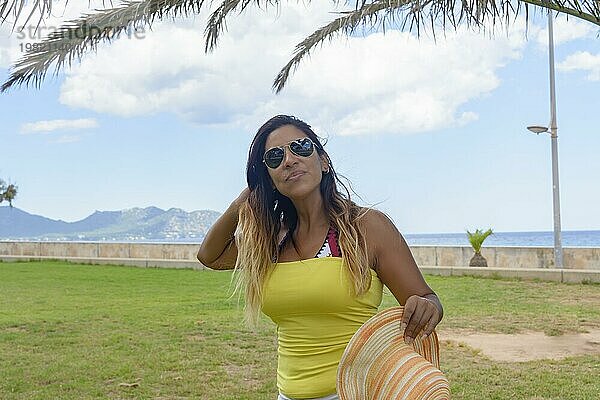 Porträt einer lateinischen Frau lächelnd  Spaß haben  im Urlaub in Mallorca posiert an einem warmen Frühling Sommer Tag  unter einer Palme  Urlaub Konzept