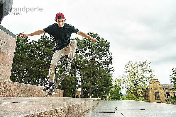 Langhaariger Skater Teenager in TShirt und Turnschuhmütze springt den Ollie vor dem Hintergrund eines stürmischen Himmels über der Stadt