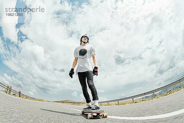 Der Typ mit dem Helm und der Sonnenbrille fährt sehr schnell mit seinem Longboard auf der Asphaltstraße in einem Ständergestell