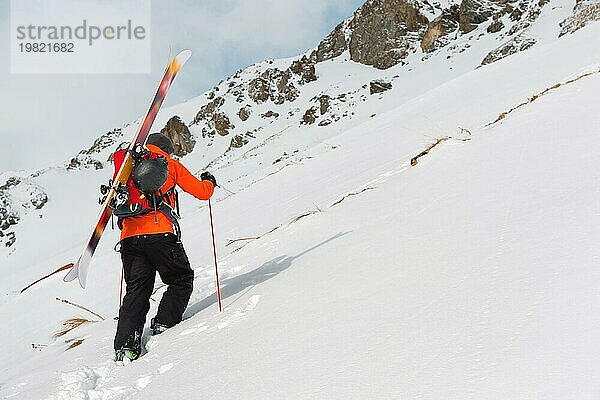 Der Ski Freerider klettert den Hang im Tiefschnee hinauf  wobei die Ausrüstung auf dem Rücken am Rucksack befestigt ist. Das Konzept des Winter Extremsports