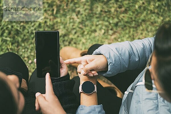 Abgeschnittene Hände einer Frau mit einer intelligenten Uhr  die auf ein Smartphone zeigt  Konzept der Technologie  soziale Netzwerke  mit zwei Personen  die etwas auf dem Smartphone anzeigen