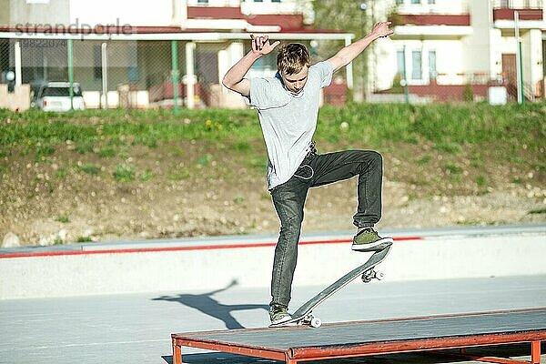 Der junge Mann gleitet auf einem Skateboard in einem Handbuch auf einer Rampe auf dem Hintergrund der Häuser