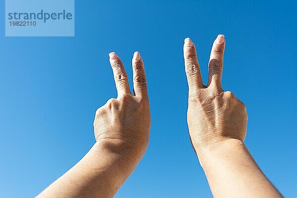 Hände einer Frau mit Victoryzeichen vor blauem Himmel im Hintergrund
