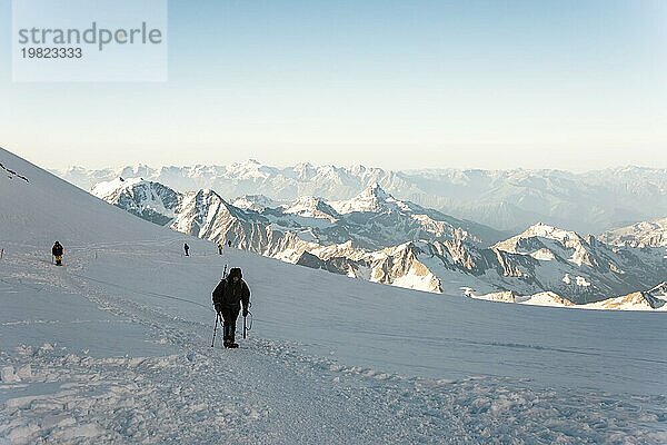 Professionelle Bergsteiger besteigen den westlichen Gipfel des Elbrus vor dem Hintergrund des kaukasischen Gebirgskamms und der schneebedeckten Gipfel des Kaukasusgebirges