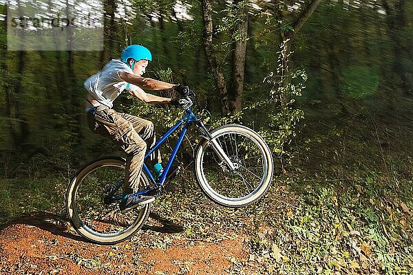 Ein junger Radfahrer mit Helm landet nach einem Sprung von einem hohen Kicker auf einem Waldradweg auf dem Fahrrad. Schießen mit langer Belichtung Verdrahtung