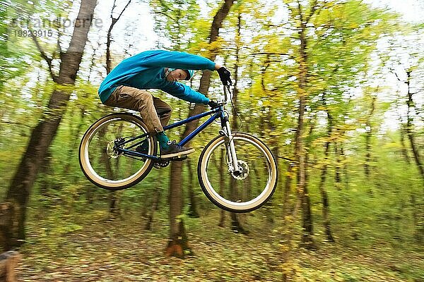 Ein junger Fahrer mit Helm und blauem Sweatshirt fliegt auf einem Fahrrad  nachdem er von einem hohen Kicker auf einem Waldradweg gesprungen ist. Aufnahme mit Langzeitbelichtung Verdrahtung