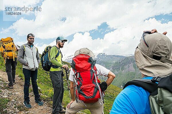 Eine Gruppe von Wanderern mit Rucksäcken und Stöcken rastet und steht in den Bergen und lauscht ihrem Führer vor dem Hintergrund der grünen und schneebedeckten Felsen