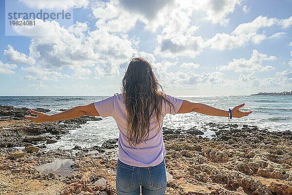 Frau mittleren Alters streckt ihre Arme aus und atmet frische Luft an der Mittelmeerküste vor der Sonne