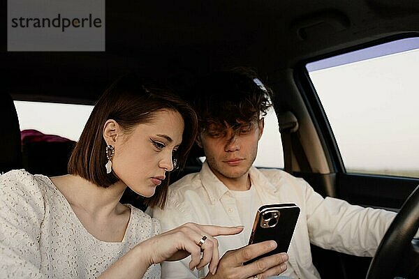 Schönes junges verliebtes Paar im Auto  das sich eine Wochenendreise auf einem Smartphone ansieht