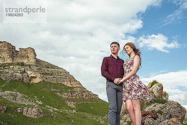 Paar Junger Mann mit einem Mädchen  das sich an den Händen hält  stehend und wegschauend im Hintergrund einer schönen Landschaft mit Felsen und Wolken. Konzept einer glücklichen jungen Familie