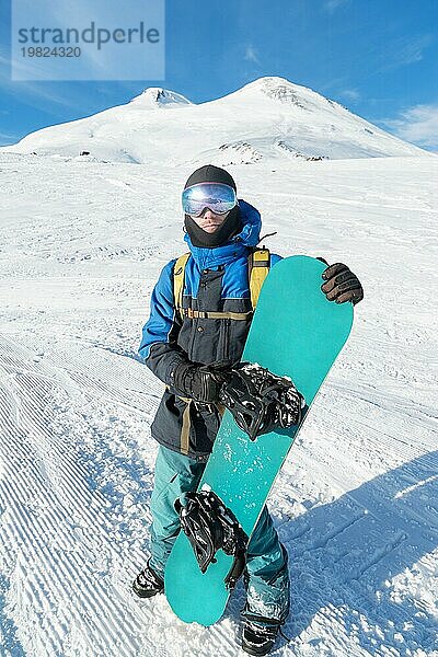 Ein professioneller Snowboarder steht mit seinem Snowboard vor dem blaün Himmel. Weitwinkel. Ansicht von unten