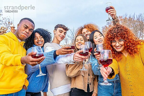 Multiethnische Freunde stoßen auf der Straße mit Rotwein an und lächeln dabei in die Kamera