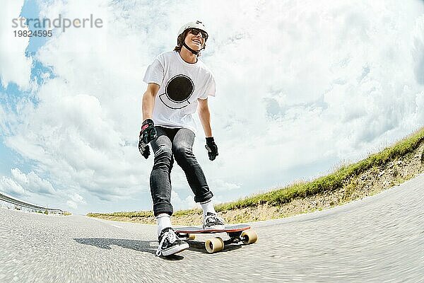 Ein junger Longboarder schiebt seinen Fuß auf seinem Longbord über die Landstraße vor dem Hintergrund der kaukasischen Landschaft